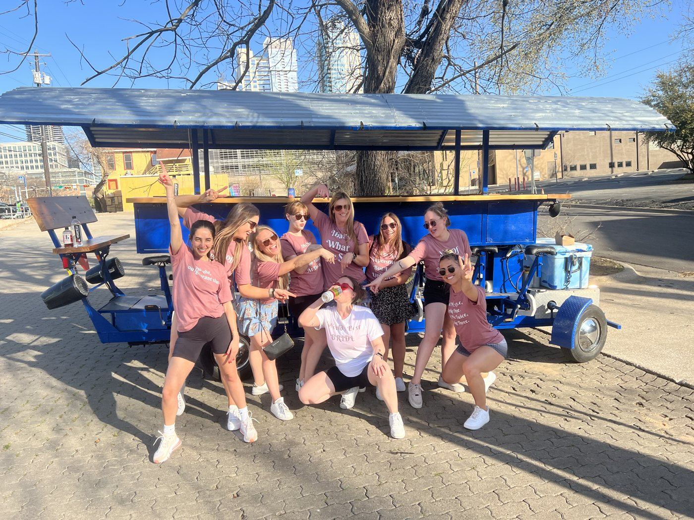 A crew posing with the blue Austin Bar Bike with the downtown skyline behind them