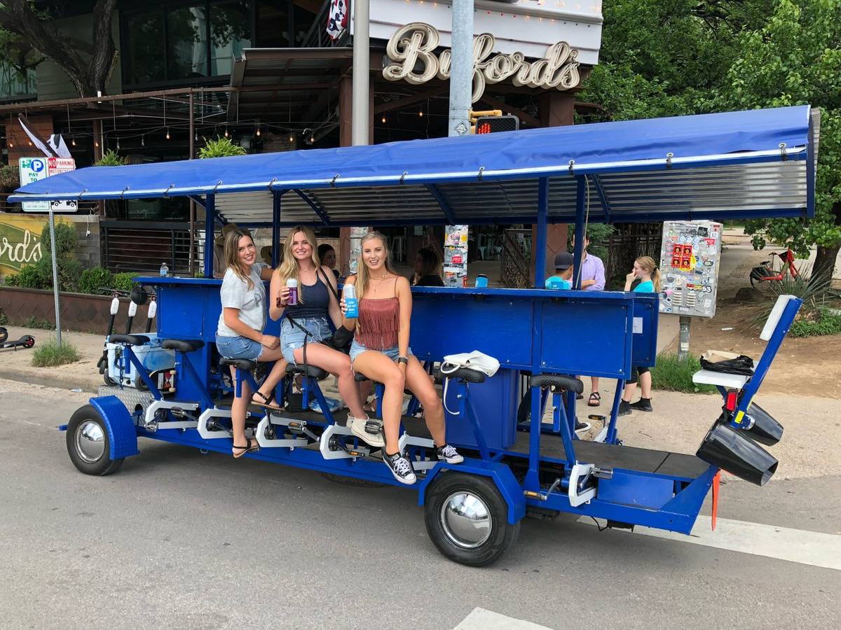 Riders with cans at the bar rail of the blue Austin beer bike