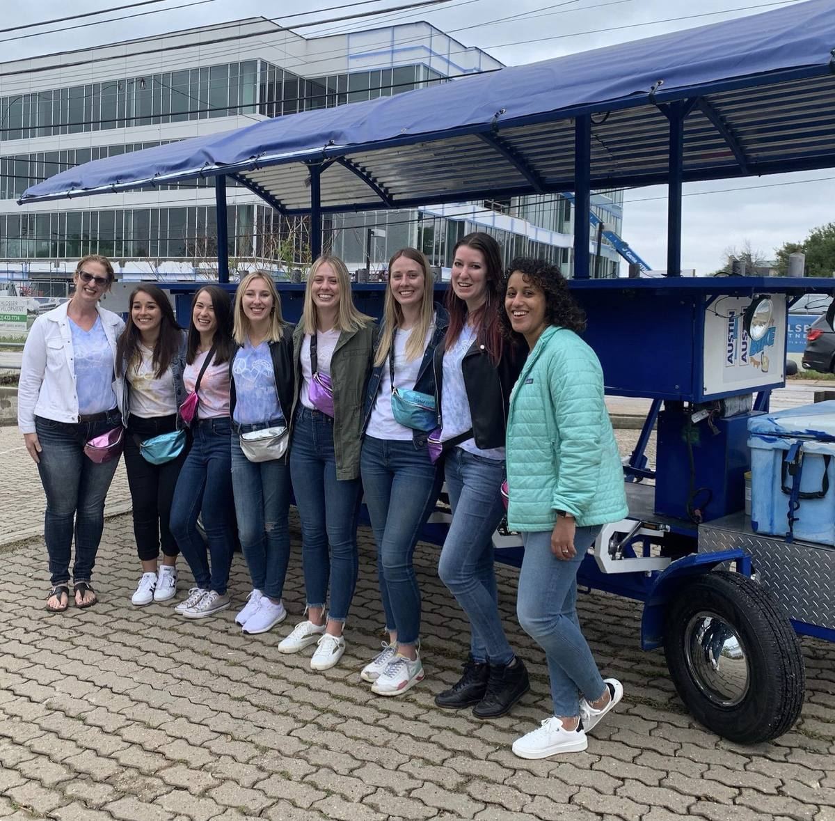 A group of friends lined up next to the blue Austin beer bike